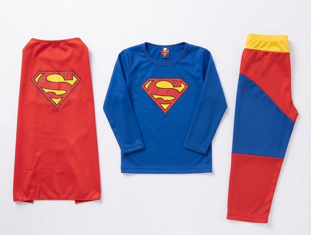 A children's three-piece Superman themed outfit laid flat on a white background, including a red cape with a yellow and red S-shield, a blue long-sleeve top with a large red and yellow S-shield on the chest, and matching pants with red, blue, and yellow color-blocked panels.