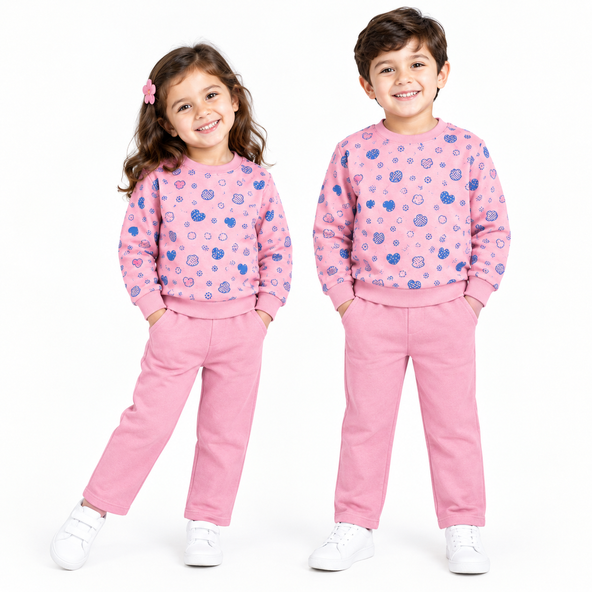 Two children modeling matching pink sweatshirt and pants sets with a blue pattern, photographed against a plain white studio background.